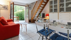 A modern living room with a red sofa, a dining table with blue chairs, a TV, and a staircase leading to a loft. - La Pommeraie by Interhome (Villers sur mer)