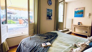 A bedroom with a bed, a bedside table, a lamp, a clock, and a painting on the wall.
