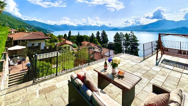 A terrace with outdoor furniture, a view of a lake, and surrounding mountains.
