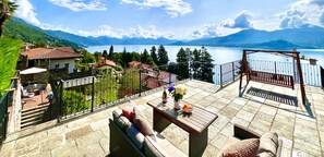 Een terras met buitenmeubilair, uitzicht op een meer en omliggende bergen.