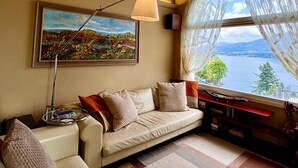 A cozy living room with a sofa, a painting, a lamp, and a view of a lake through a window.