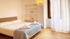 A neatly made bed with a striped blanket, a headboard, and a shelf with a decorative item and a candle. - Eva Apartament with Lake View in Baveno (Baveno)