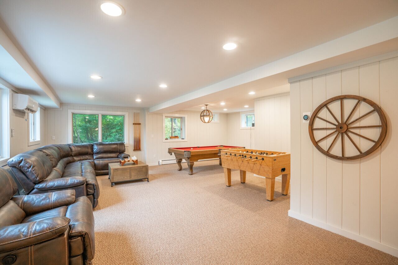 A spacious room with a leather sofa, a pool table, and a foosball table.