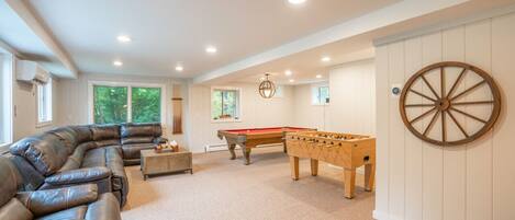A spacious room with a leather sofa, a pool table, and a foosball table.