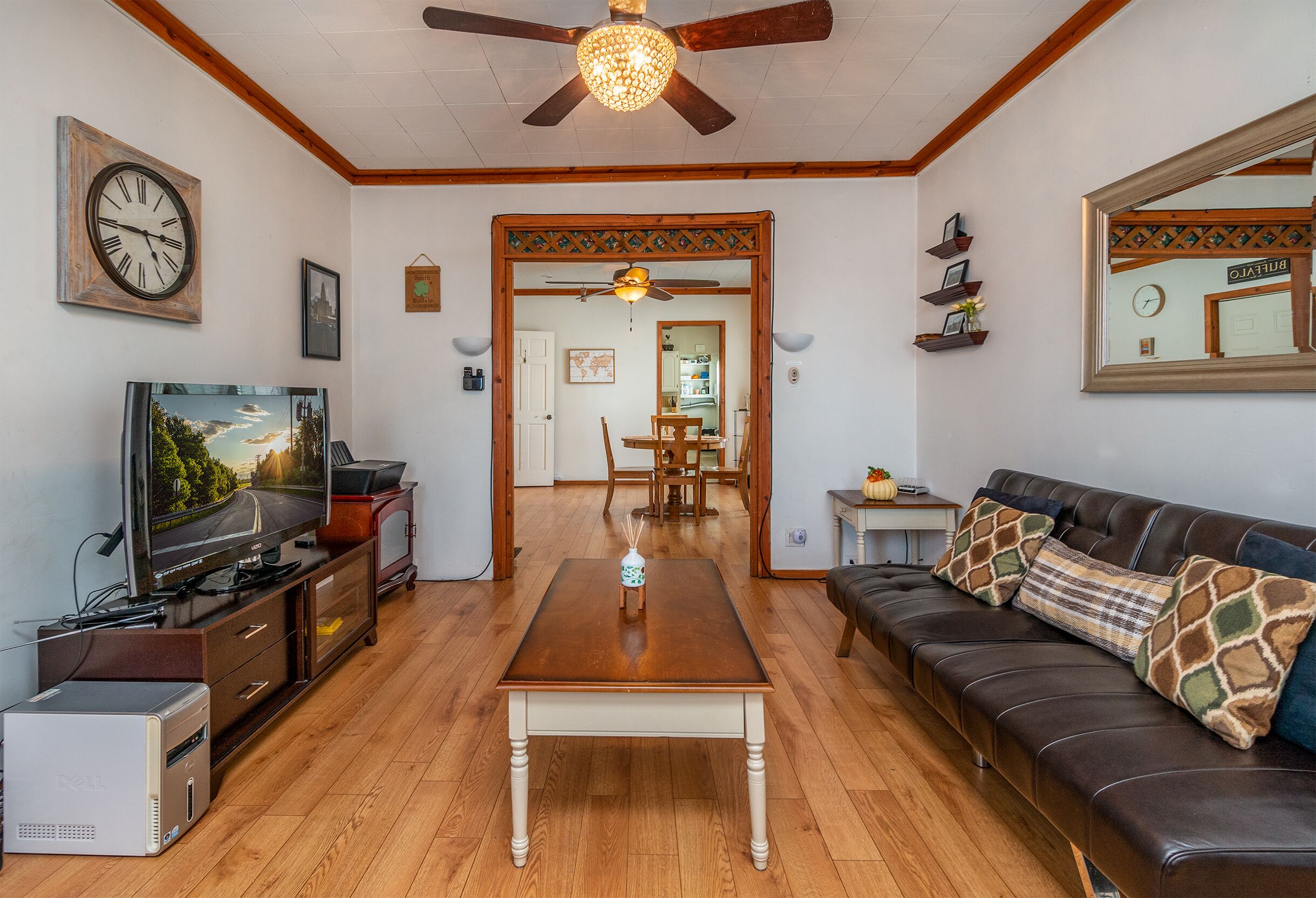 A living room with a wooden floor, a television, a coffee table, a sofa, a ceiling fan, and a clock on the wall.