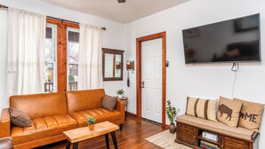 Un salon avec un canapé en cuir, une table basse en bois, un téléviseur fixé au mur et une porte dotée d’un miroir.
