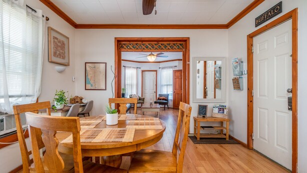 Un coin repas avec une table et des chaises en bois, un ventilateur de plafond et une porte portant l’inscription « BUFFALO ».