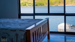 Un dormitorio con un ventanal grande que da a un lago, un bote y una zona boscosa.