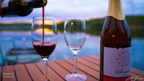 Una botella de vino sirviendo en una copa, con otra copa vacía y una mesa de madera al frente.