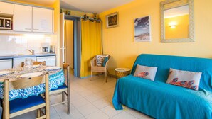 A compact living space with a kitchen area, a dining table with chairs, a sofa, and a small side table.