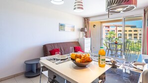 A modern kitchen with a dining area, a balcony with a view of buildings, and a large window.