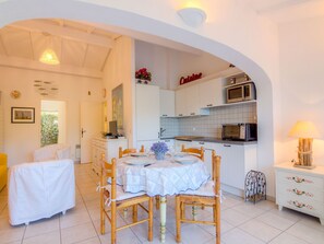 A bright, open-plan living and dining area with a kitchen, white walls, and a dining table set for four.