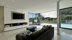Una sala de estar moderna con un televisor de pantalla plana grande, un sofá y una mesa de vidrio.
