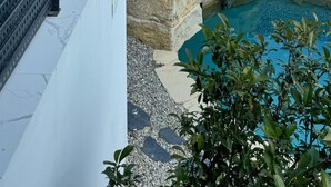 Un edificio moderno con amplias ventanas, un área de piscina con formaciones rocosas y vistas a árboles y colinas al fondo.