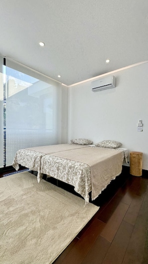 A modern bedroom with a large bed, a window, and an air conditioning unit.