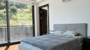Un dormitorio moderno con una cama grande, un tapete blanco y vistas al verdor exterior.