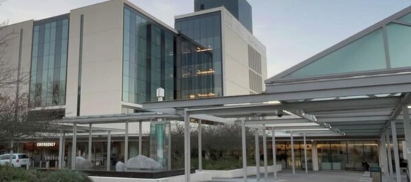 Un edificio moderno con fachada de vidrio, un área de entrada cubierta y un cartel que indica una salida de emergencia.