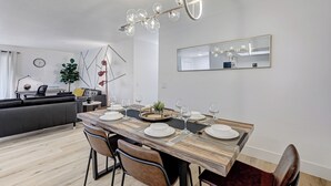 Ett modernt matområde med ett träbord som är dukat för sex personer, omgivet av stolar. En stor spegel och en unik kristallkrona syns på väggarna.