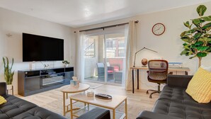 Ett modernt vardagsrum med en platt-TV, en soffa, ett soffbord och en skjutdörr i glas som leder ut till ett utomhusområde.