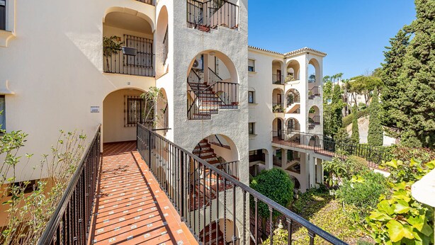 Un immeuble à plusieurs étages doté de balcons, d’un escalier central et entouré de verdure.