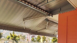 Ein überdachter Außenbereich mit Metallveranda, einer Backsteinmauer und Blick auf eine Straße sowie Gebäude im Hintergrund.