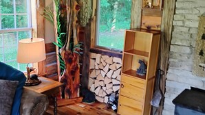 Een rustiek houten interieur met houten vloer, een open haard, een lamp en een raam met uitzicht op groen.