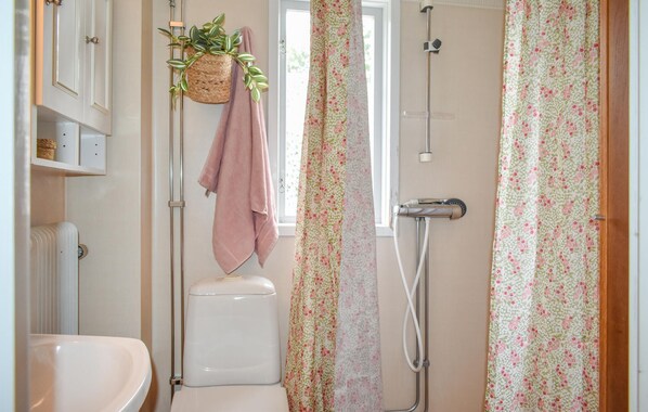 Un baño con inodoro, una planta colgante, ducha y cortinas con motivos florales.