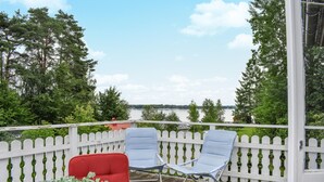 A deck with two chairs and a potted plant, overlooking a lake with trees and a distant shoreline.