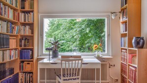 A study with a large window, wooden bookshelves, a radiator, and a desk with a chair.