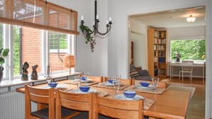 A dining area with a table set for four, surrounded by wooden chairs with dark cushions.