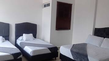A hotel room with two single beds and a larger bed, all with headboards and white bedding.