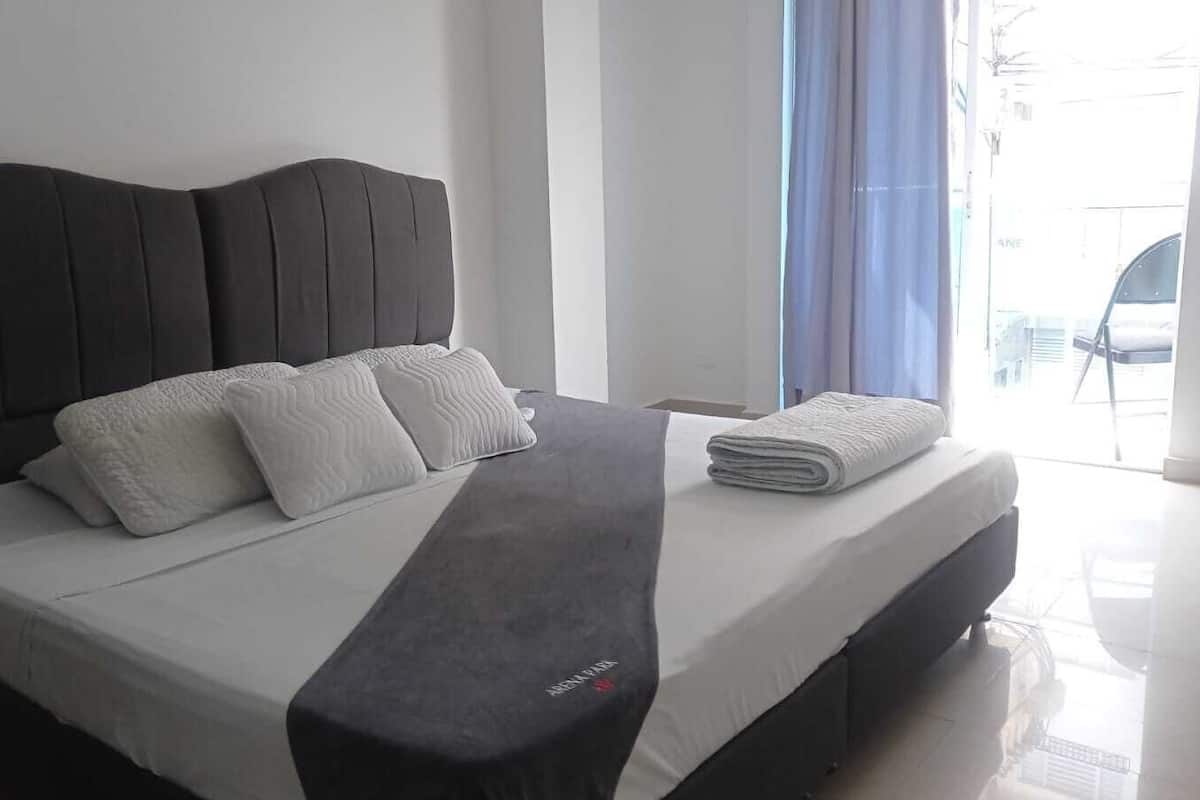 Een moderne hotelkamer met een groot bed, een grijze hoofdeinde en uitzicht op de straat door een raam.