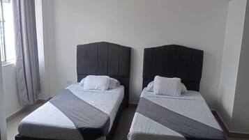 Une chambre avec deux lits, chacun doté d’une tête de lit sombre et de draps blancs.