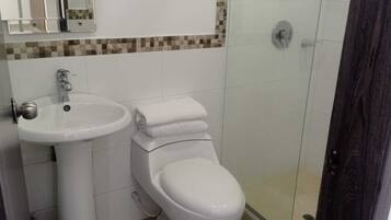Une salle de bain avec un lavabo, des toilettes et une douche, le tout de couleur blanche.