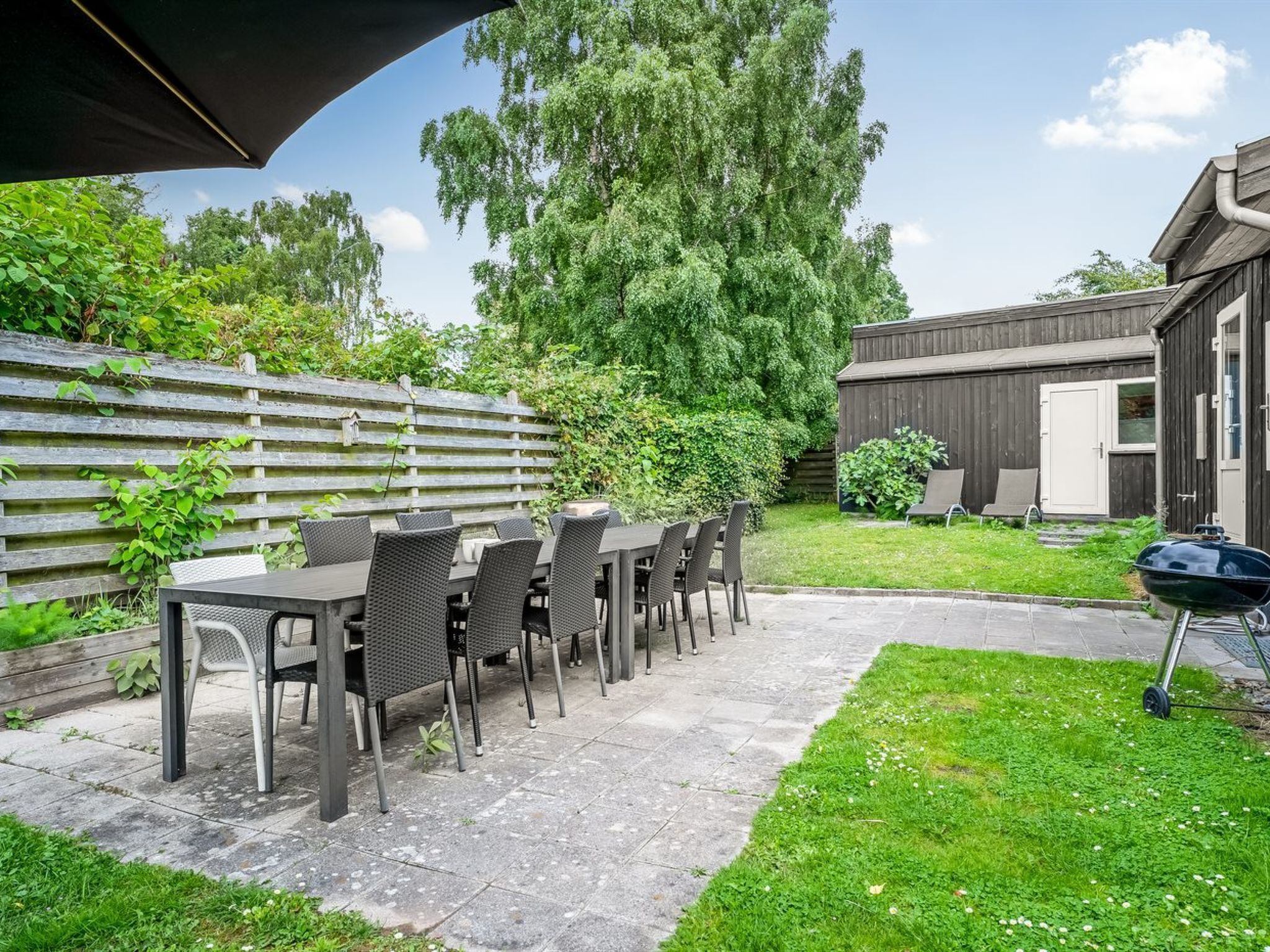 An outdoor patio with a table and chairs, a barbecue grill, and a wooden fence.