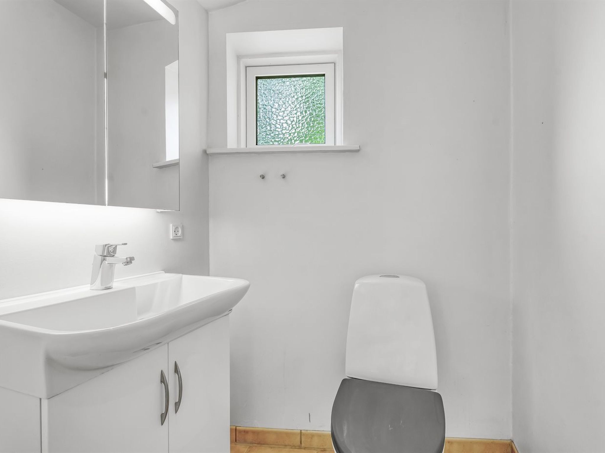 A modern bathroom with a white sink, mirror, and toilet.