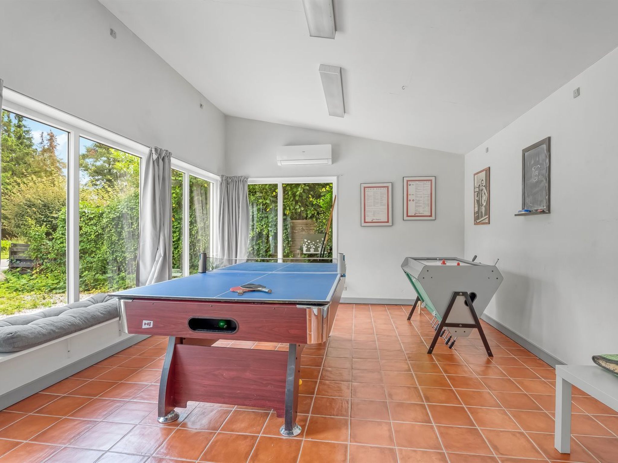 Een kamer met een pooltafel, een biljarttafel en grote ramen met uitzicht op groen.