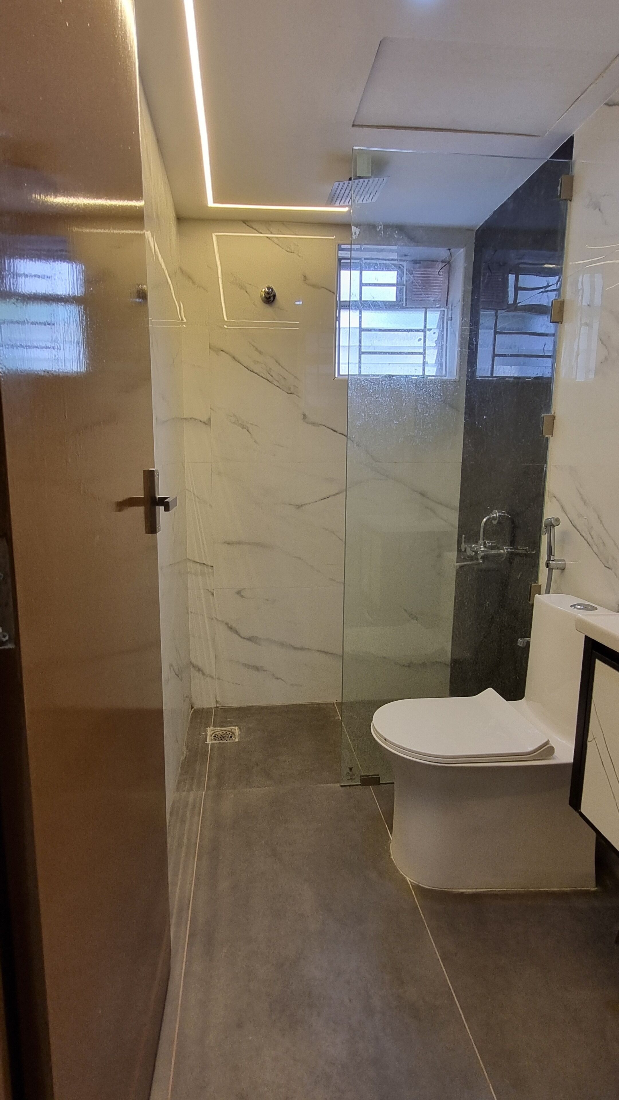 A modern bathroom with a glass-enclosed shower, a white toilet, and a marble wall.