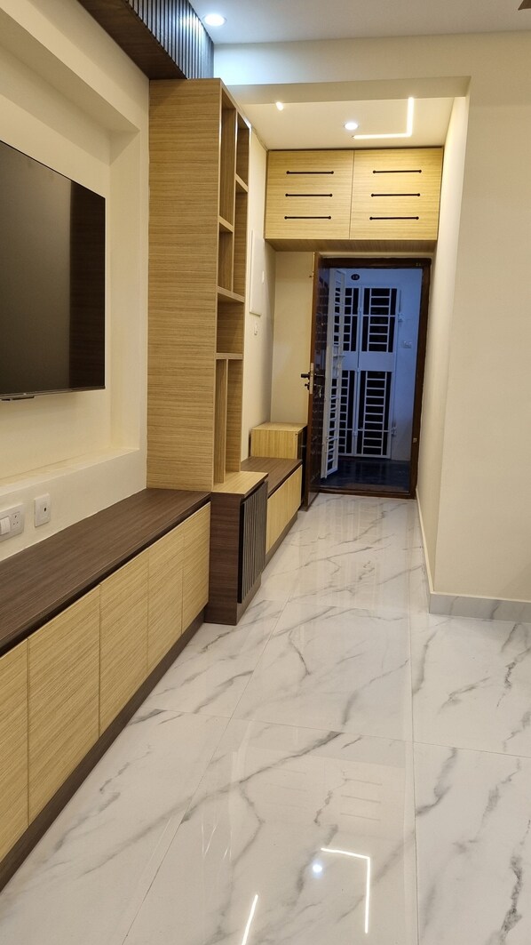 A modern hallway with a wooden cabinet, a built-in TV, and a marble floor.