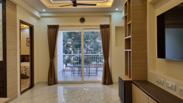A modern living room with a large TV, a balcony with a railing, and a ceiling fan. - Airport Inn  (Chennai)
