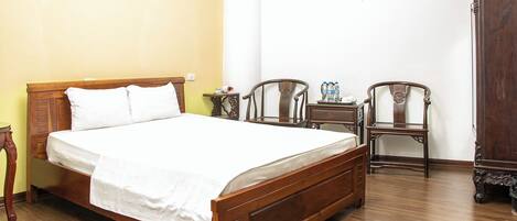 A wooden bed with white linens, two wooden chairs, a small table with water bottles, and a wooden wardrobe.