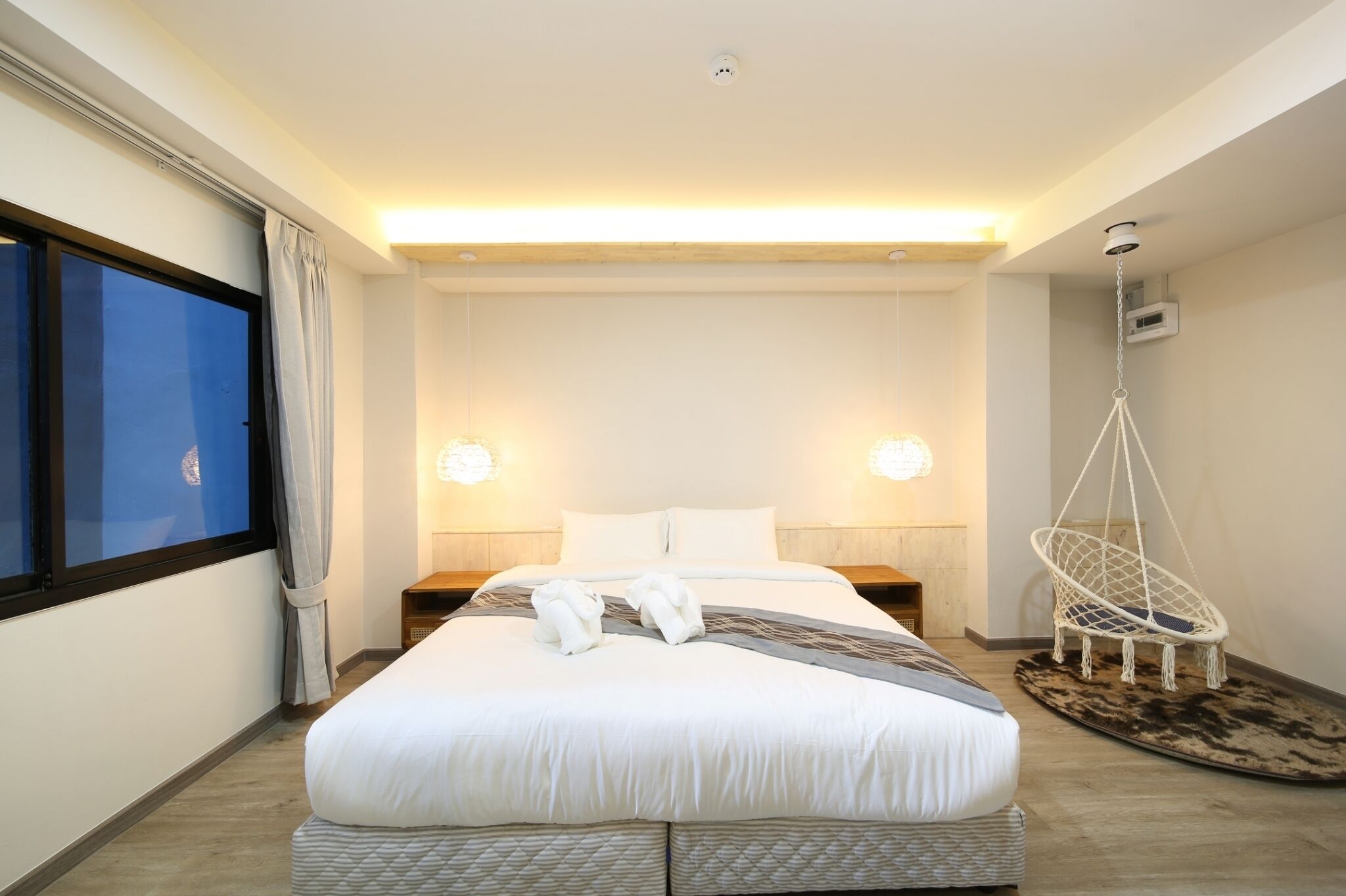 A hotel room with a large bed, bedside lamps, a hanging chair, and a view of the city.