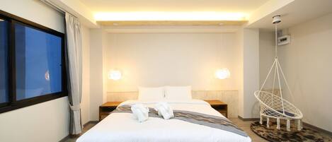 A hotel room with a large bed, bedside lamps, a hanging chair, and a view of the city.