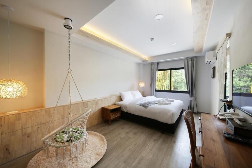 A modern hotel room with a bed, desk, hanging chair, and large window.