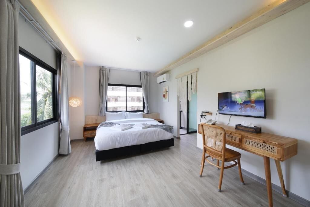 Habitación de hotel moderna con una cama grande, un escritorio con silla, un televisor y un ventanal con cortinas.
