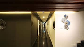 A hallway with a modern design, featuring a dark floor, a ceiling with horizontal lines, and a wall-mounted decorative piece.