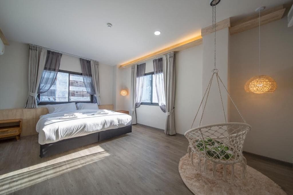Un dormitorio moderno con una cama, una silla colgante y un ventanal con cortinas.