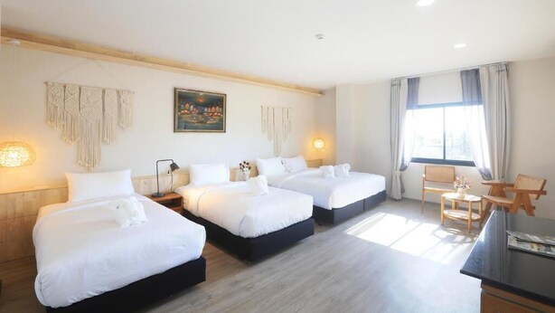 Une chambre d’hôtel avec trois lits, un bureau, une chaise et une fenêtre avec des rideaux.