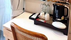 Une chambre d’hôtel avec un bureau en bois, une chaise, un plateau avec des tasses à thé, une bouilloire et des bouteilles.