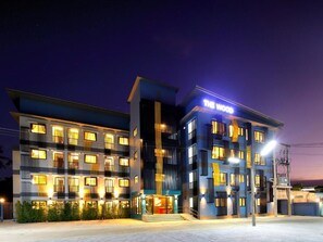 Un hotel de varios pisos con el rótulo 'The Wood', una escalera central y una fachada bien iluminada.